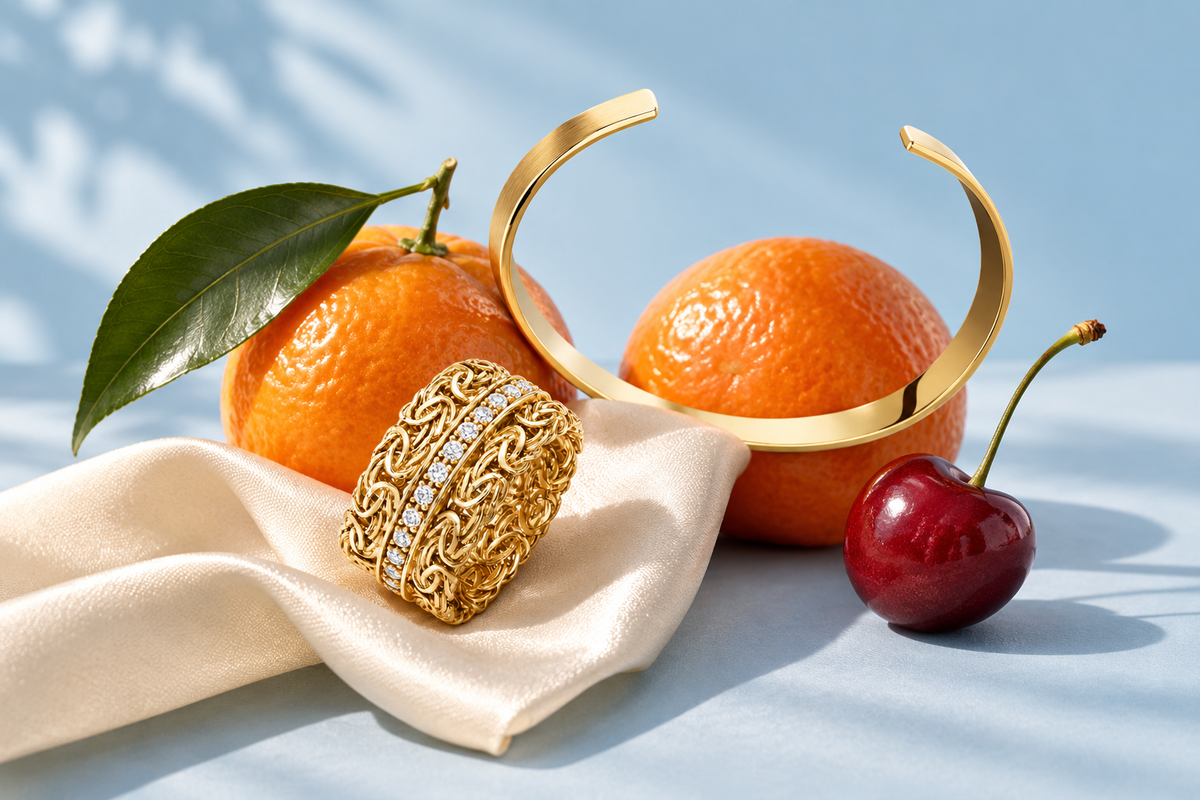 All Tied Up gold ring and Power Couple cuff styled with mandarins, a cherry and ivory satin on a pale blue background
