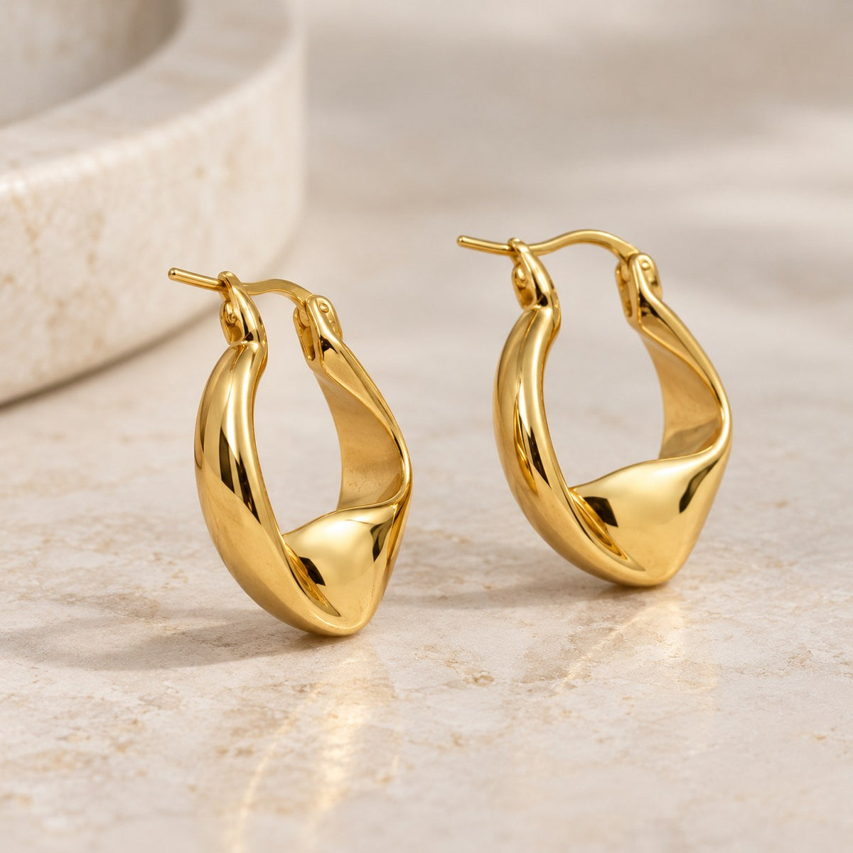 Plot Twist twisted gold hoop earrings styled on a travertine ledge