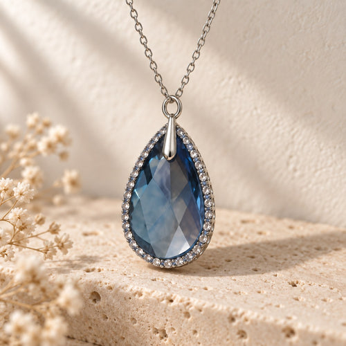 Blue Chip denim blue crystal teardrop pendant in sterling silver on a travertine ledge
