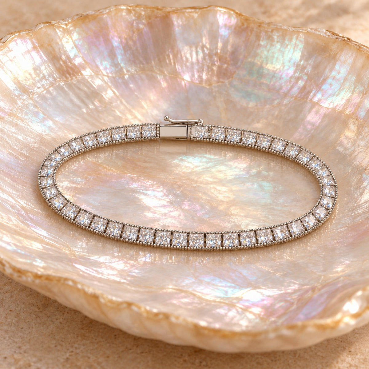 Fair and Square tennis bracelet on a shell dish — square princess-cut stones with a beaded edge, box clasp closed