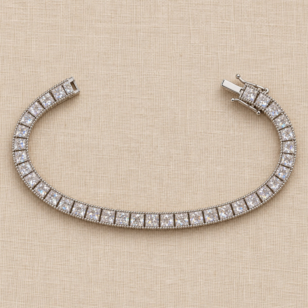 Fair and Square tennis bracelet full length on linen — square princess-cut stones with a beaded edge, box clasp
