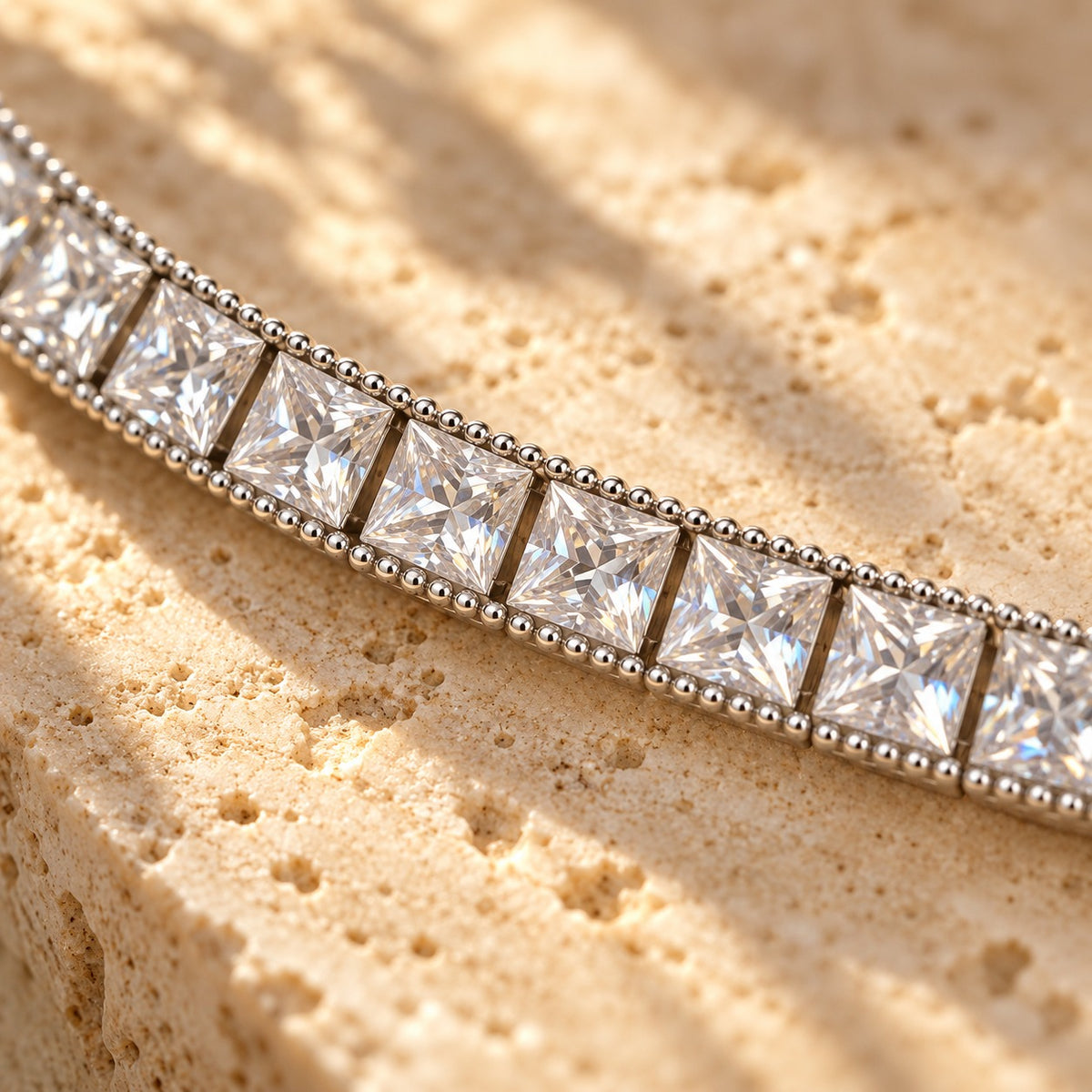 Fair and Square close-up — square princess-cut stones framed by a beaded silver edge on travertine