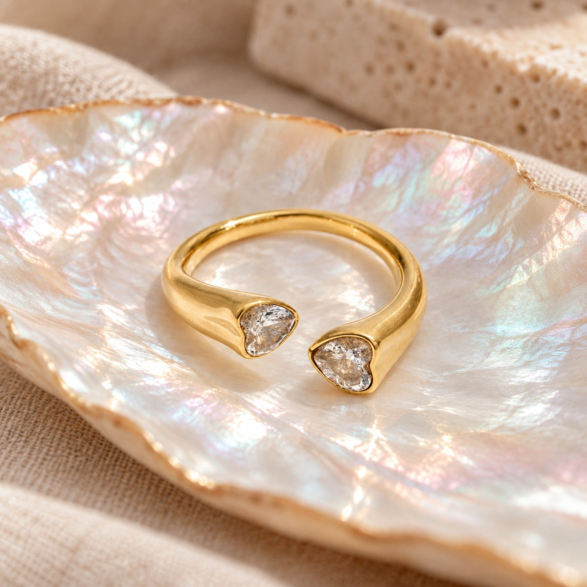 Twin Heart open gold ring with two heart-shaped stones on an iridescent shell dish